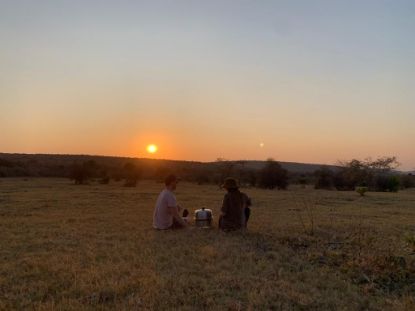 two people sitting on grass cooking on the Cobb Premier Air portable charcoal cooker